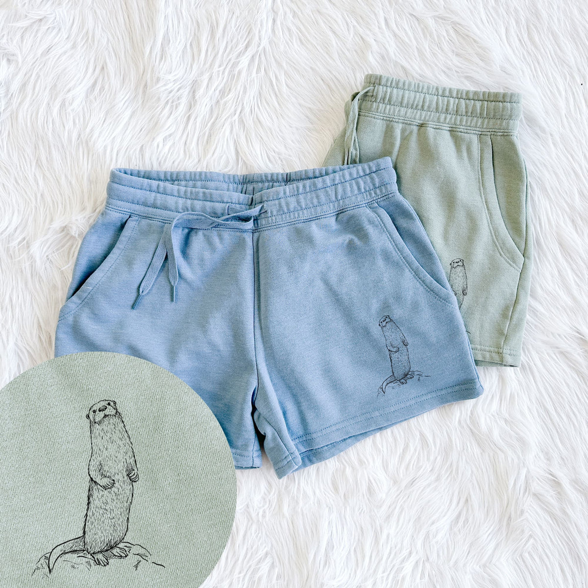 Two pairs of Cali Wave shorts in different colors printed with a black ink illustration of a river otter standing upright on a rock, with a close-up of the print.