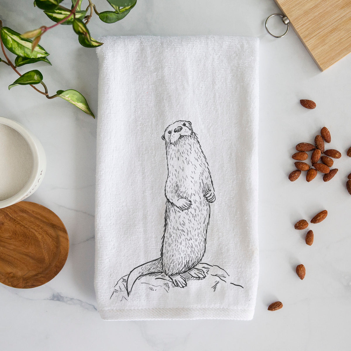 White hand towel printed with a black ink illustration of a river otter standing upright on a rock.
