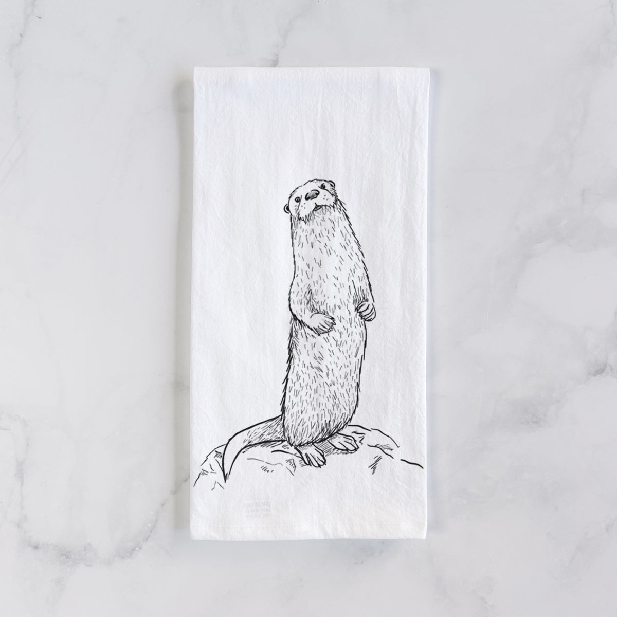 White cotton tea towel laid flat on marble, printed with a black ink illustration of a river otter standing upright on a rock.