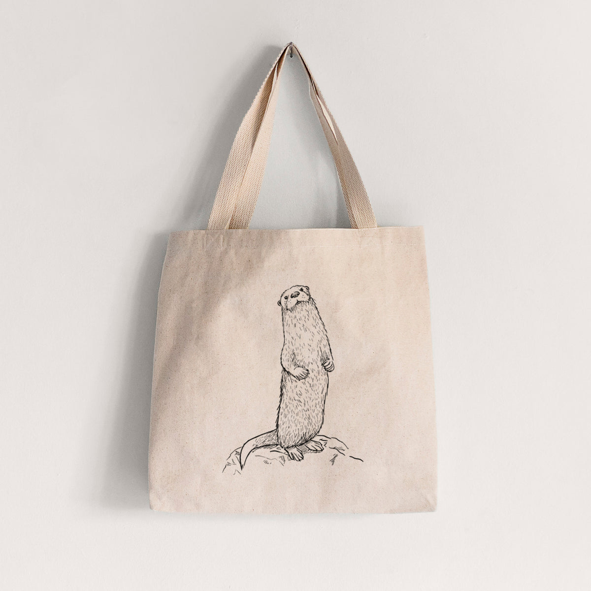Natural canvas tote bag printed with a black ink illustration of a river otter standing upright on a rock.