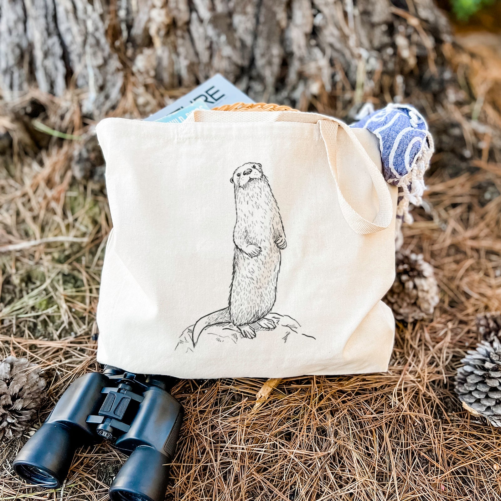 Natural canvas tote bag printed with a black ink illustration of a river otter standing upright on a rock.