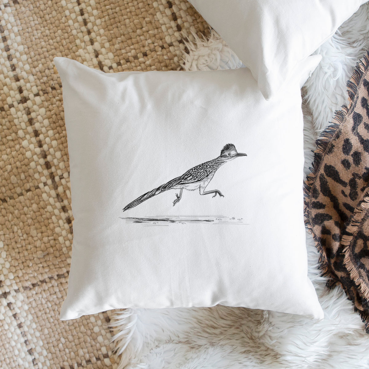 White pillow cover printed with a black ink illustration of a roadrunner running, on a woven chair.
