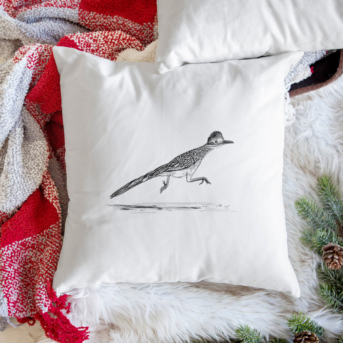 White pillow cover printed with a black ink illustration of a roadrunner running, on a woven chair.