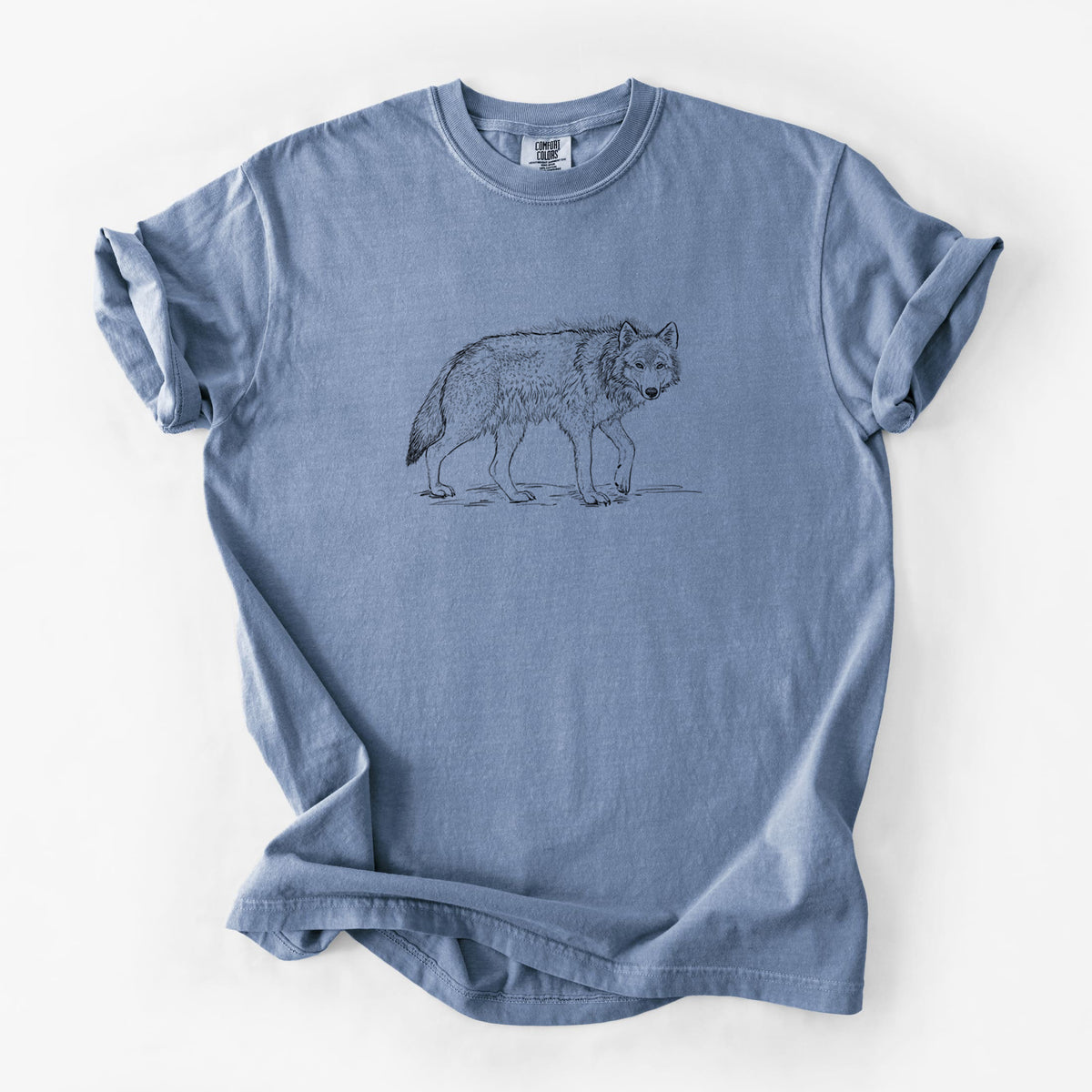 Blue jean Comfort Colors t-shirt laid flat, printed with a detailed black ink illustration of a grey wolf walking.