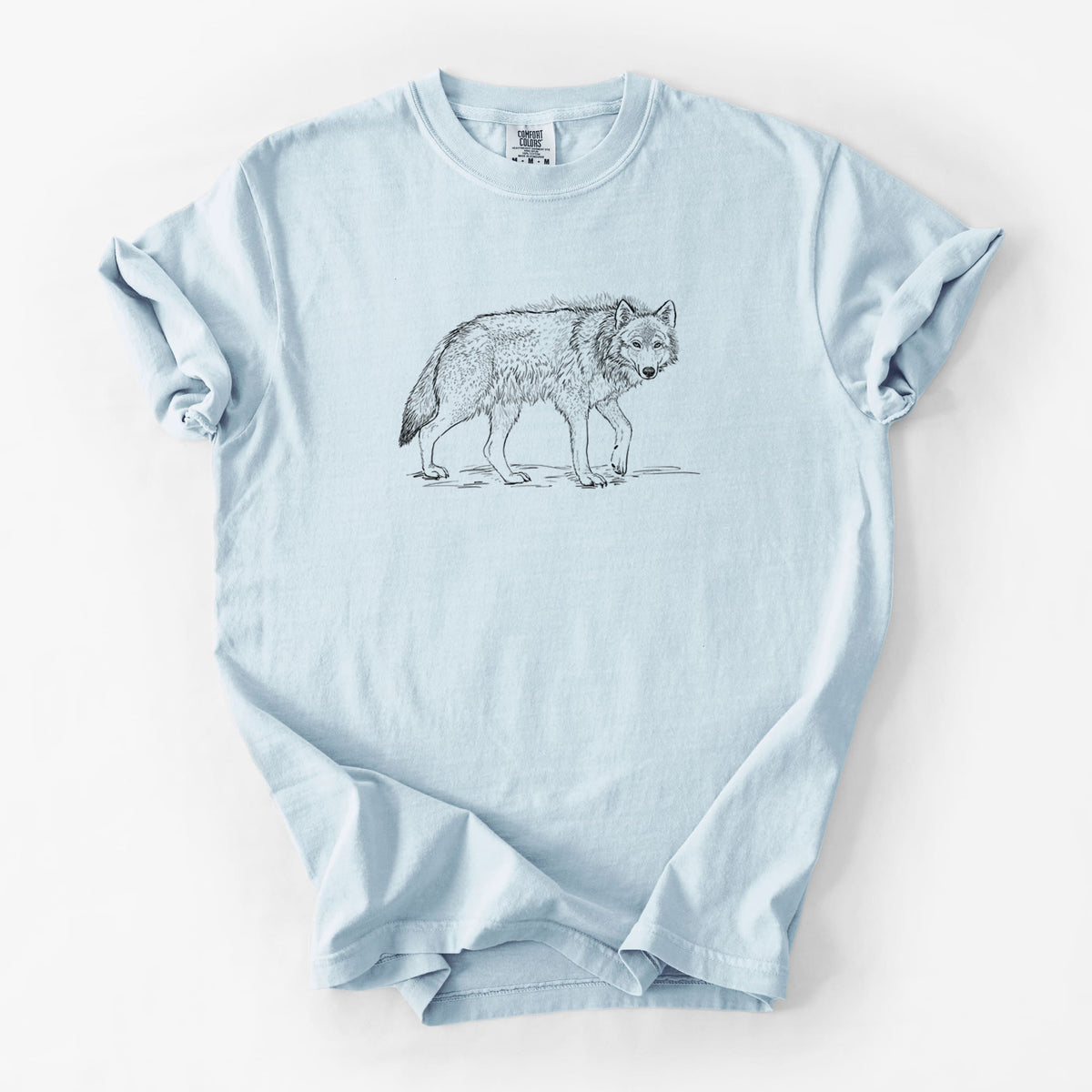 Chambray blue Comfort Colors t-shirt laid flat, printed with a detailed black ink illustration of a grey wolf walking.