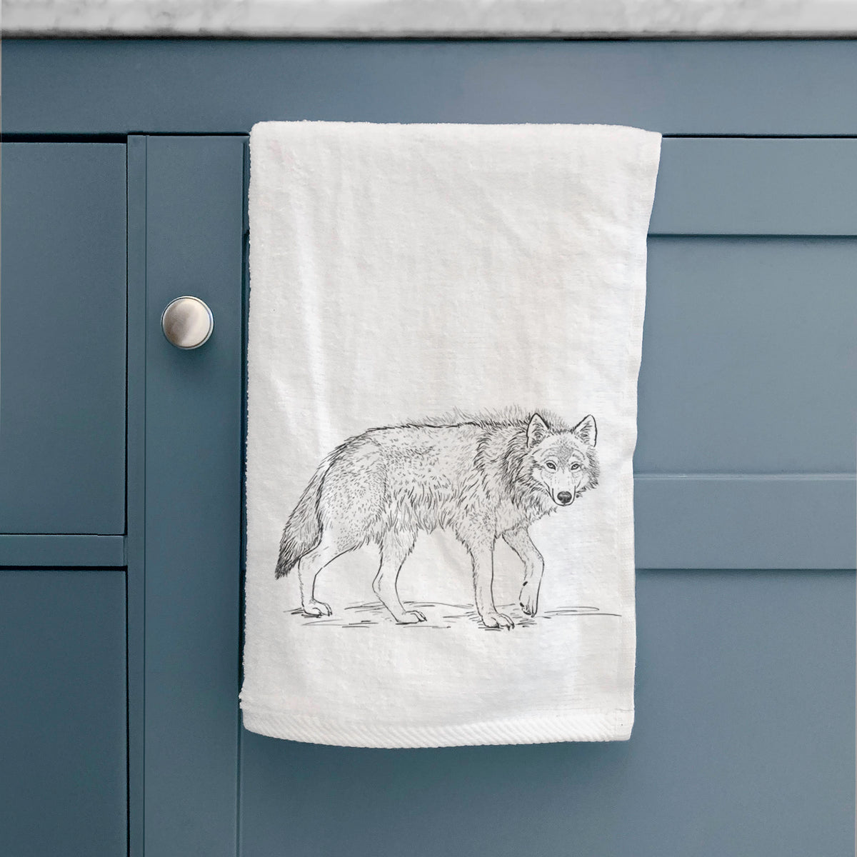 White hand towel printed with a detailed black ink illustration of a grey wolf walking, hanging on a cabinet door.