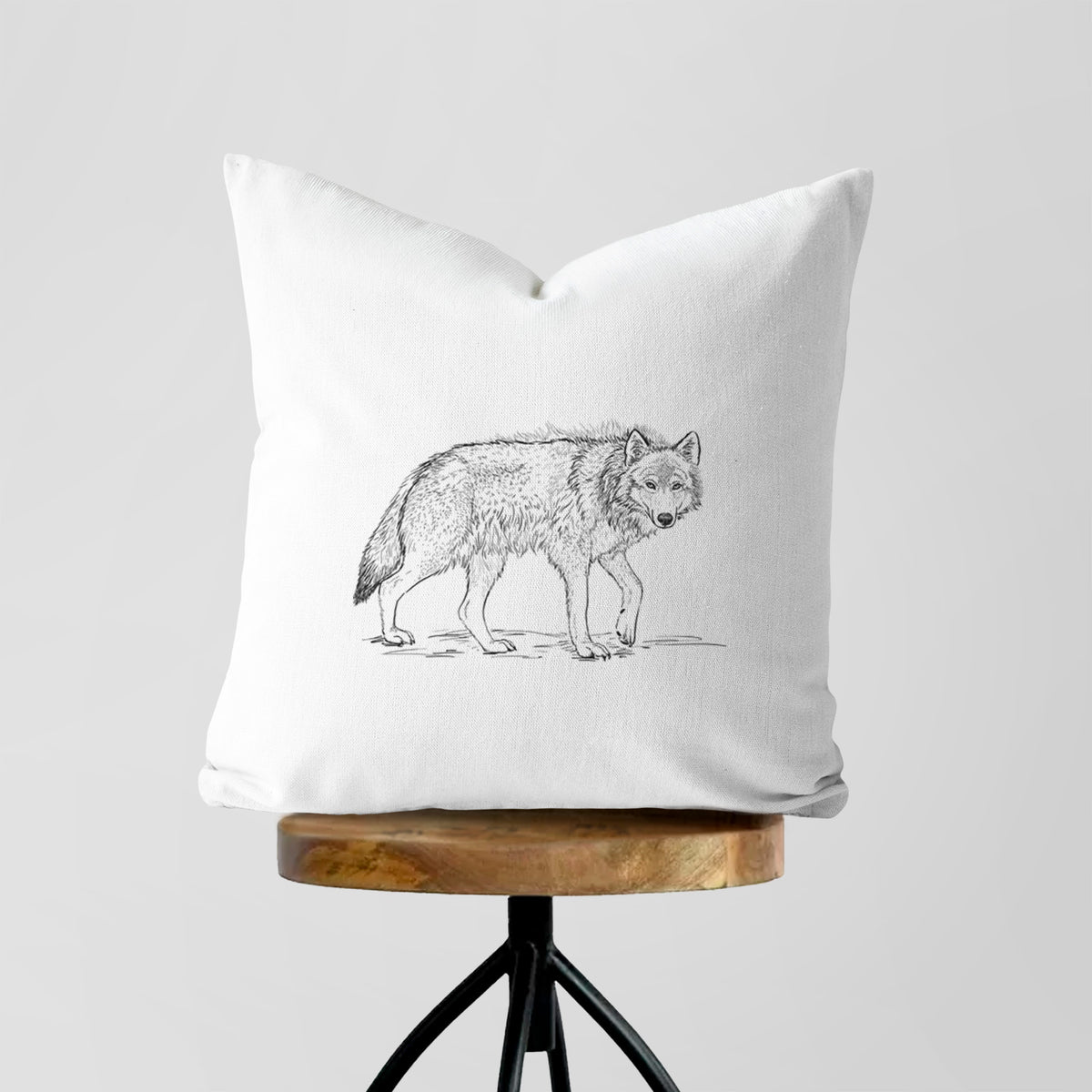 White pillow cover printed with a detailed black ink illustration of a grey wolf walking, on a wooden stool.
