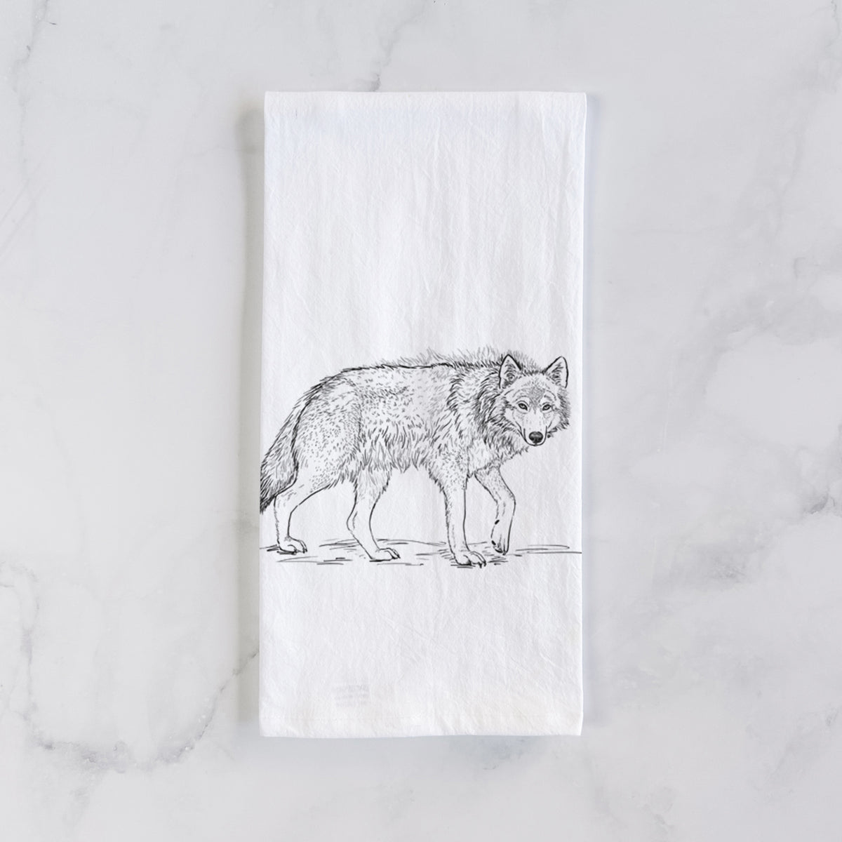 White cotton tea towel laid flat on marble, printed with a detailed black ink illustration of a grey wolf walking.