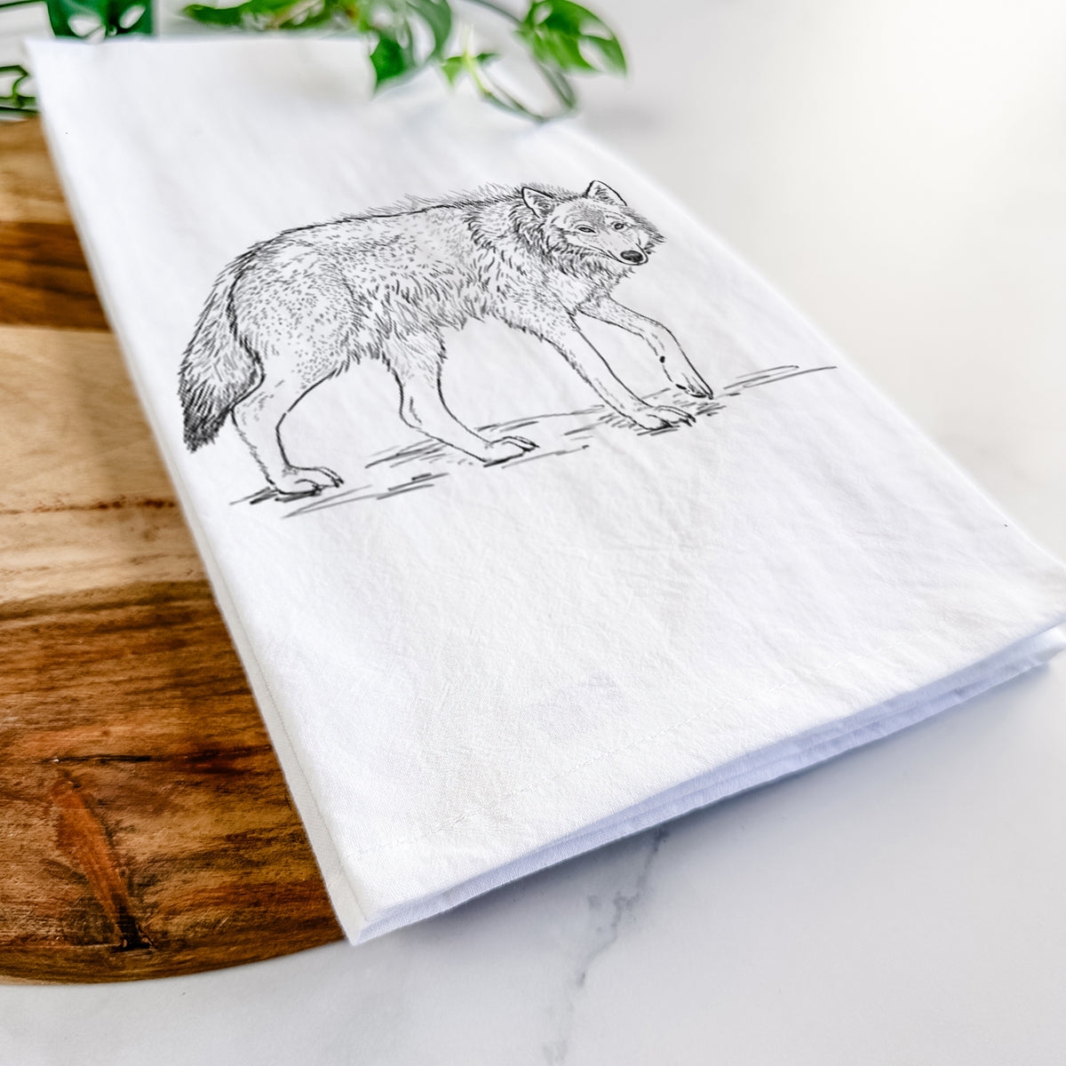 Close-up of a folded white tea towel on a wooden board, showing a detailed black ink illustration of a grey wolf walking.