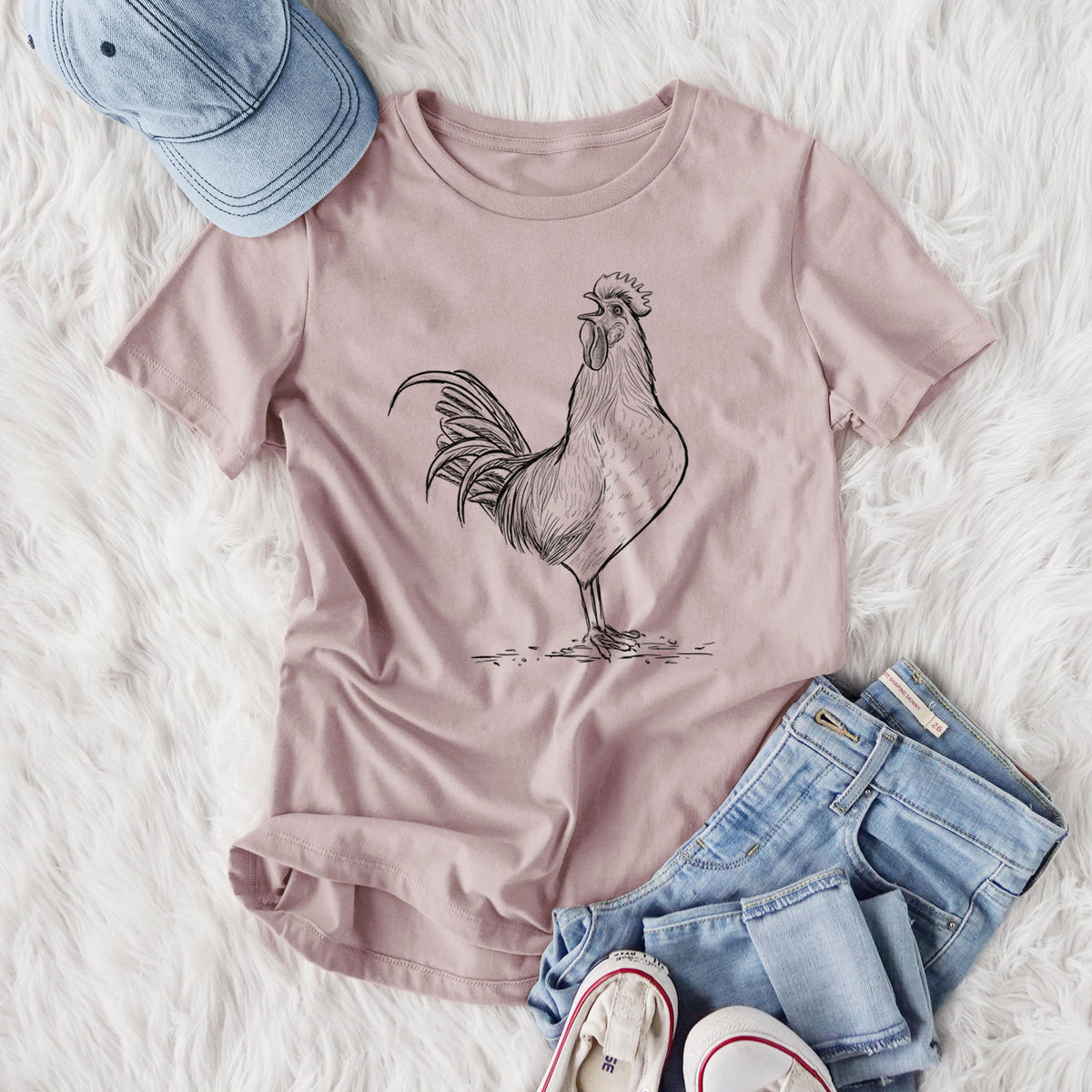 Women's relaxed fit cotton t-shirt printed with a detailed black ink illustration of a rooster crowing, styled flat on a white faux fur rug with jeans.