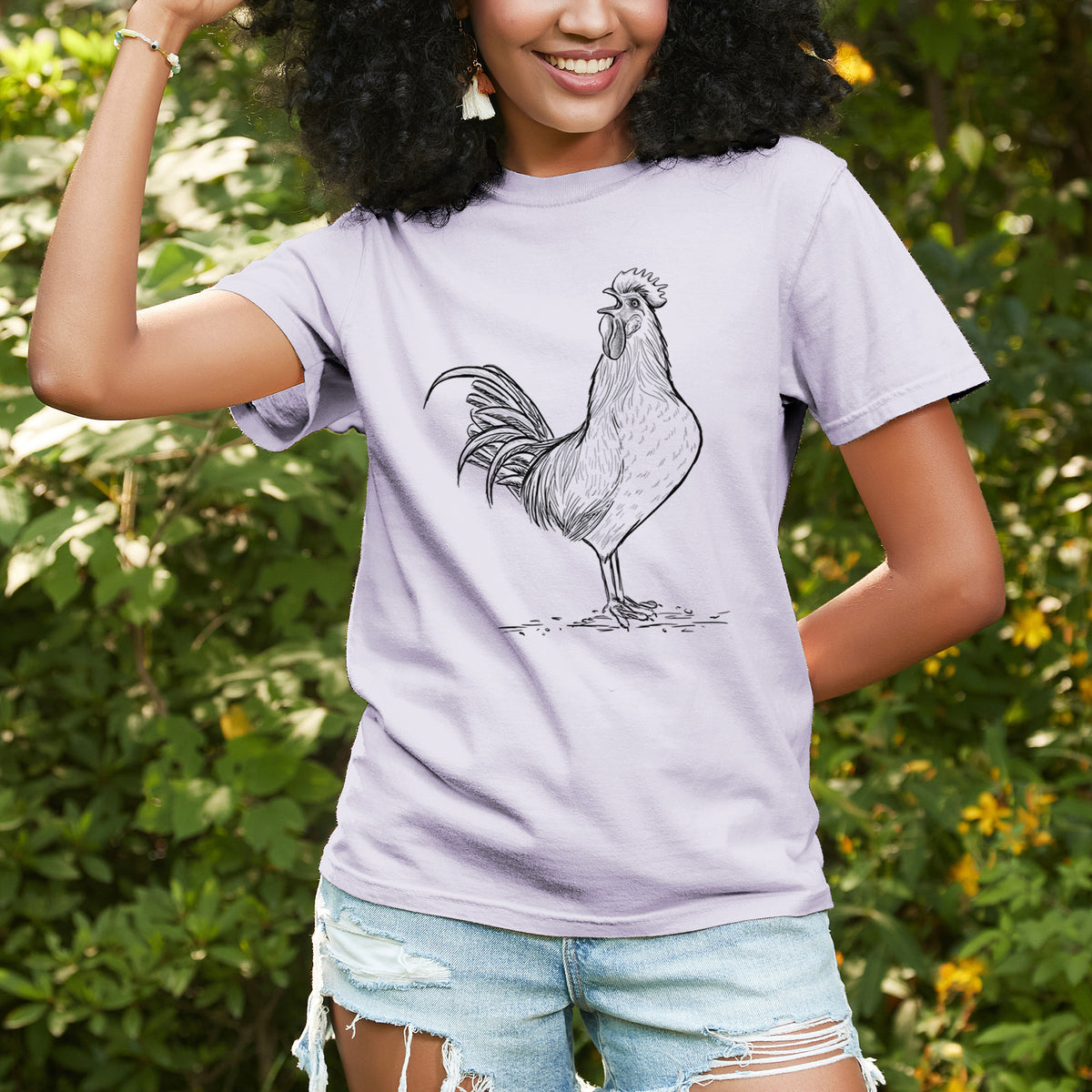 Woman wearing a Comfort Colors t-shirt printed with a detailed black ink illustration of a rooster crowing, outdoors.