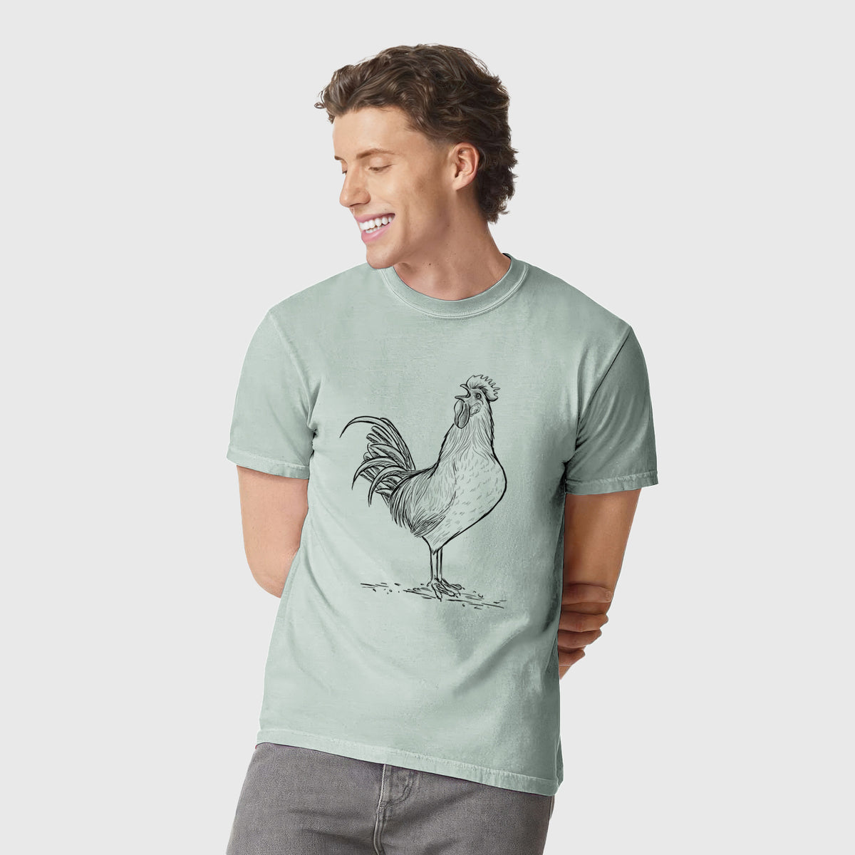 Man wearing a Comfort Colors t-shirt printed with a detailed black ink illustration of a rooster crowing.