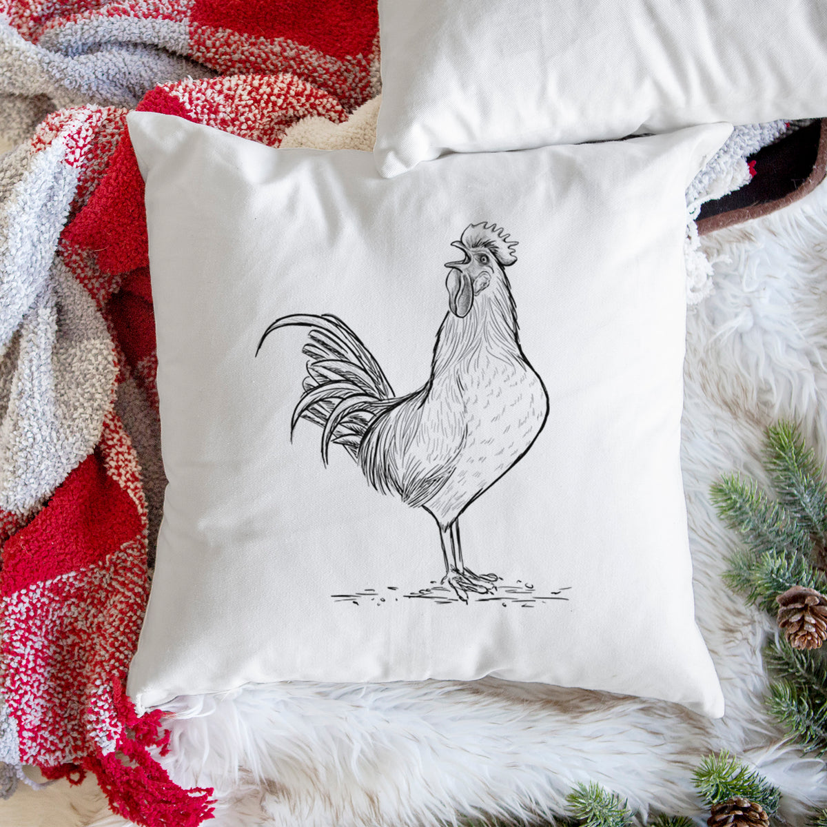 White pillow cover printed with a detailed black ink illustration of a rooster crowing, on a woven chair.