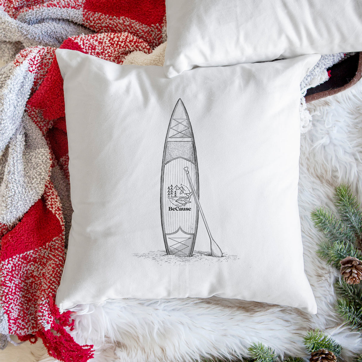 White pillow cover printed with a black ink illustration of a stand-up paddleboard with a paddle, on a woven chair.
