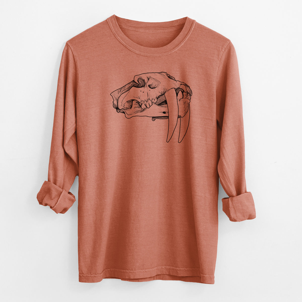 Yam burnt orange Comfort Colors long sleeve shirt laid flat with the cuffs rolled, printed with a detailed black ink illustration of a saber-toothed tiger skull.