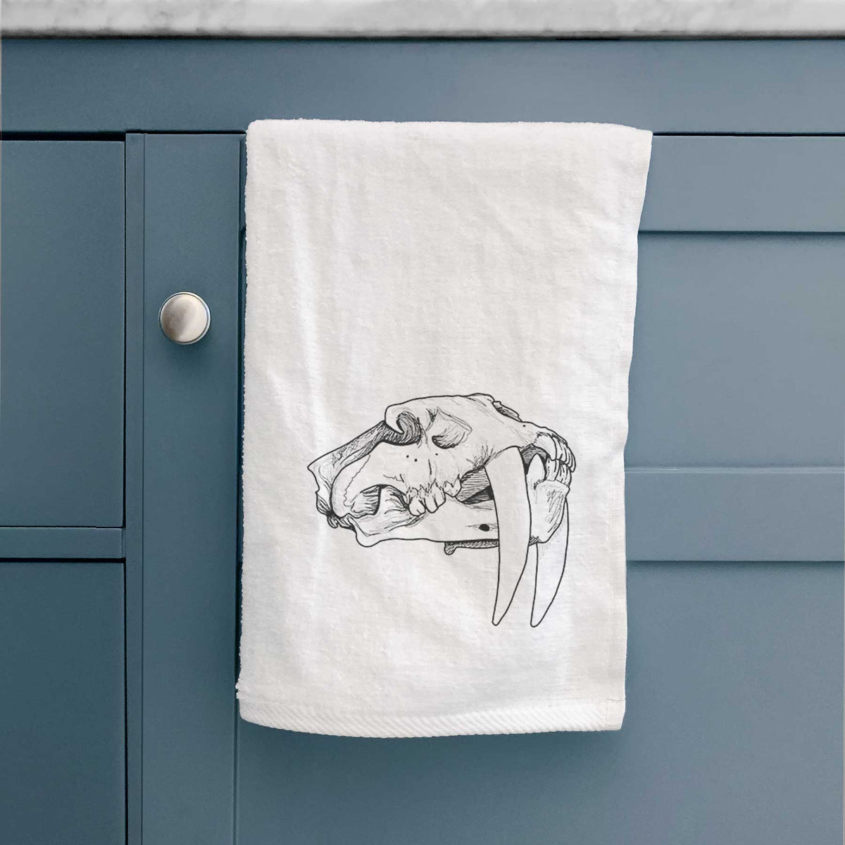 White hand towel printed with a detailed black ink illustration of a saber-toothed tiger skull.