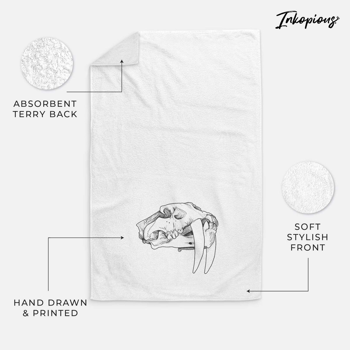 White hand towel printed with a detailed black ink illustration of a saber-toothed tiger skull.