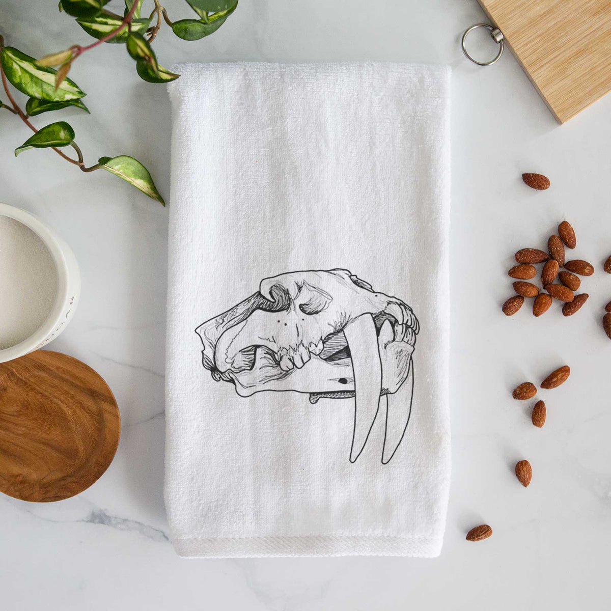 White hand towel printed with a detailed black ink illustration of a saber-toothed tiger skull.