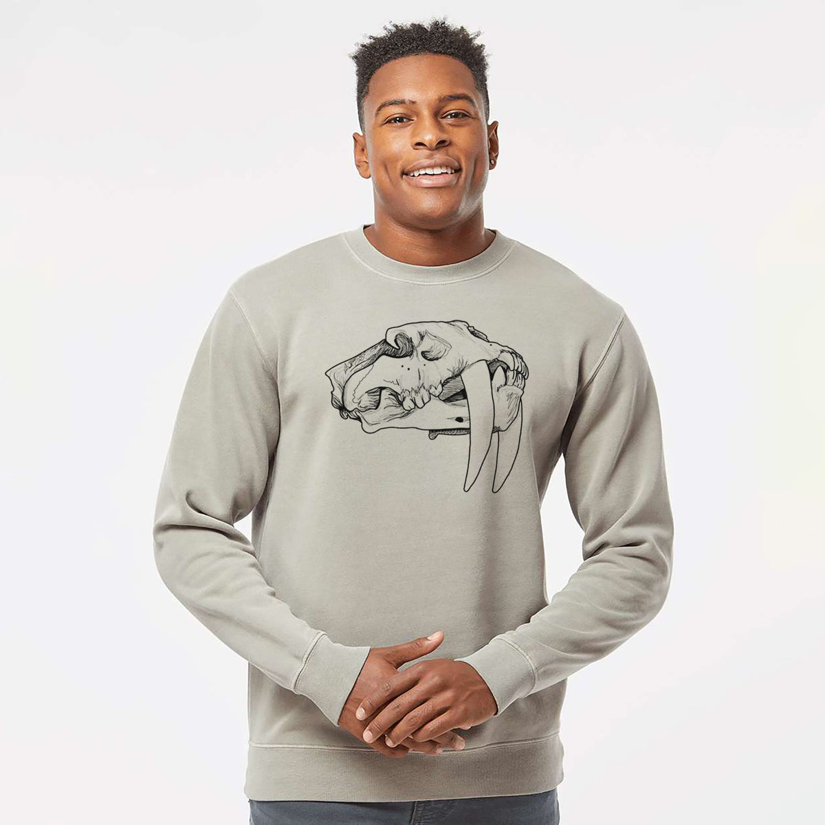 Model wearing a cement grey pigment dyed crewneck sweatshirt printed with a detailed black ink illustration of a saber-toothed tiger skull.