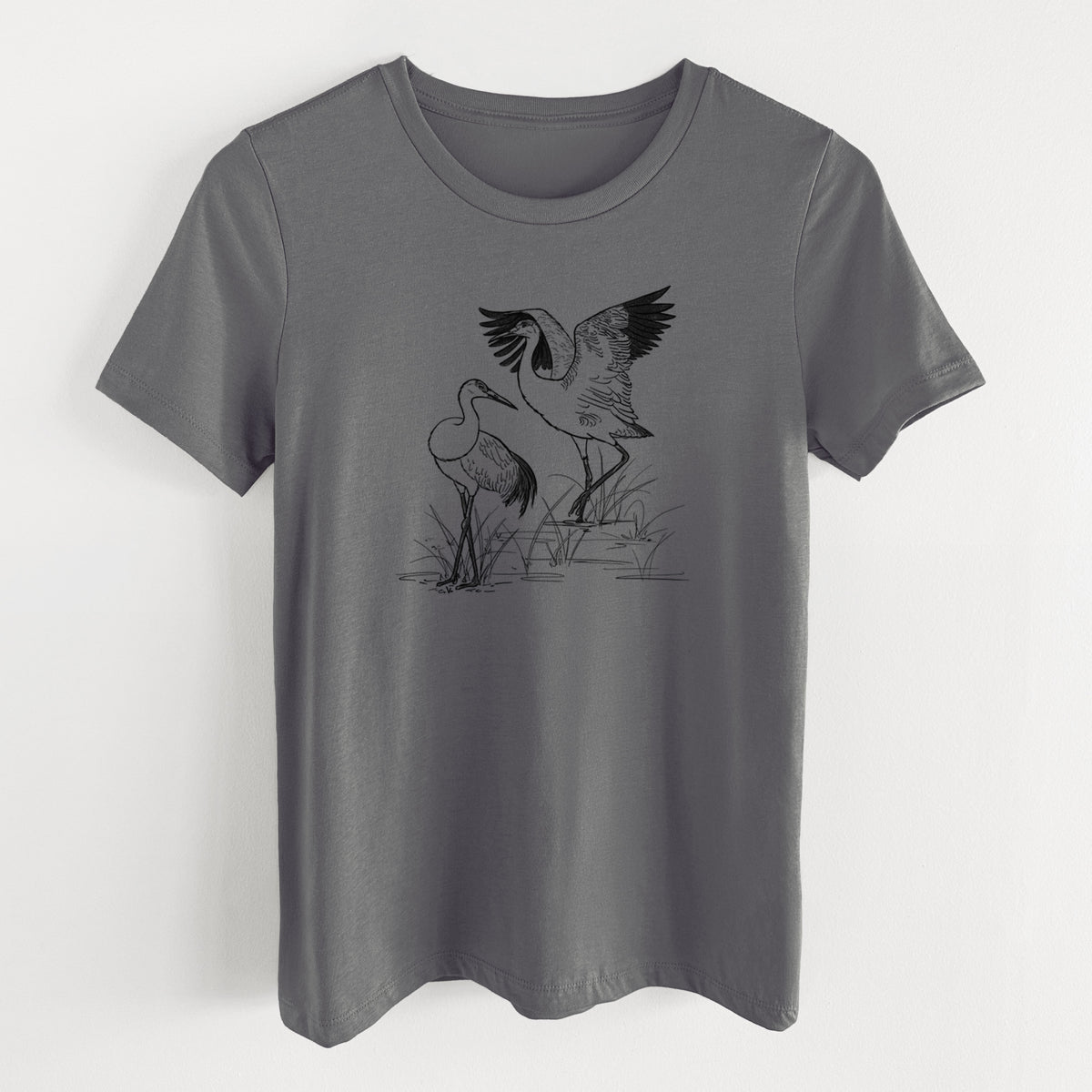 Asphalt women's relaxed fit cotton t-shirt laid flat, printed with a black ink illustration of two sandhill cranes in marsh grass, one with its wings raised.