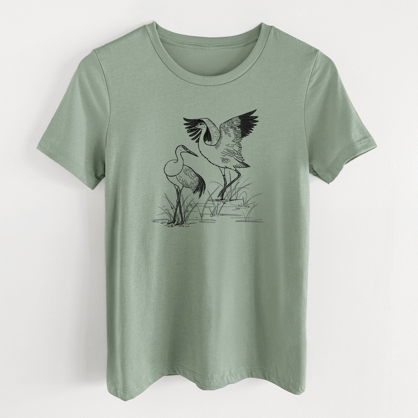 Sage green women's relaxed fit cotton t-shirt laid flat, printed with a black ink illustration of two sandhill cranes in marsh grass, one with its wings raised.