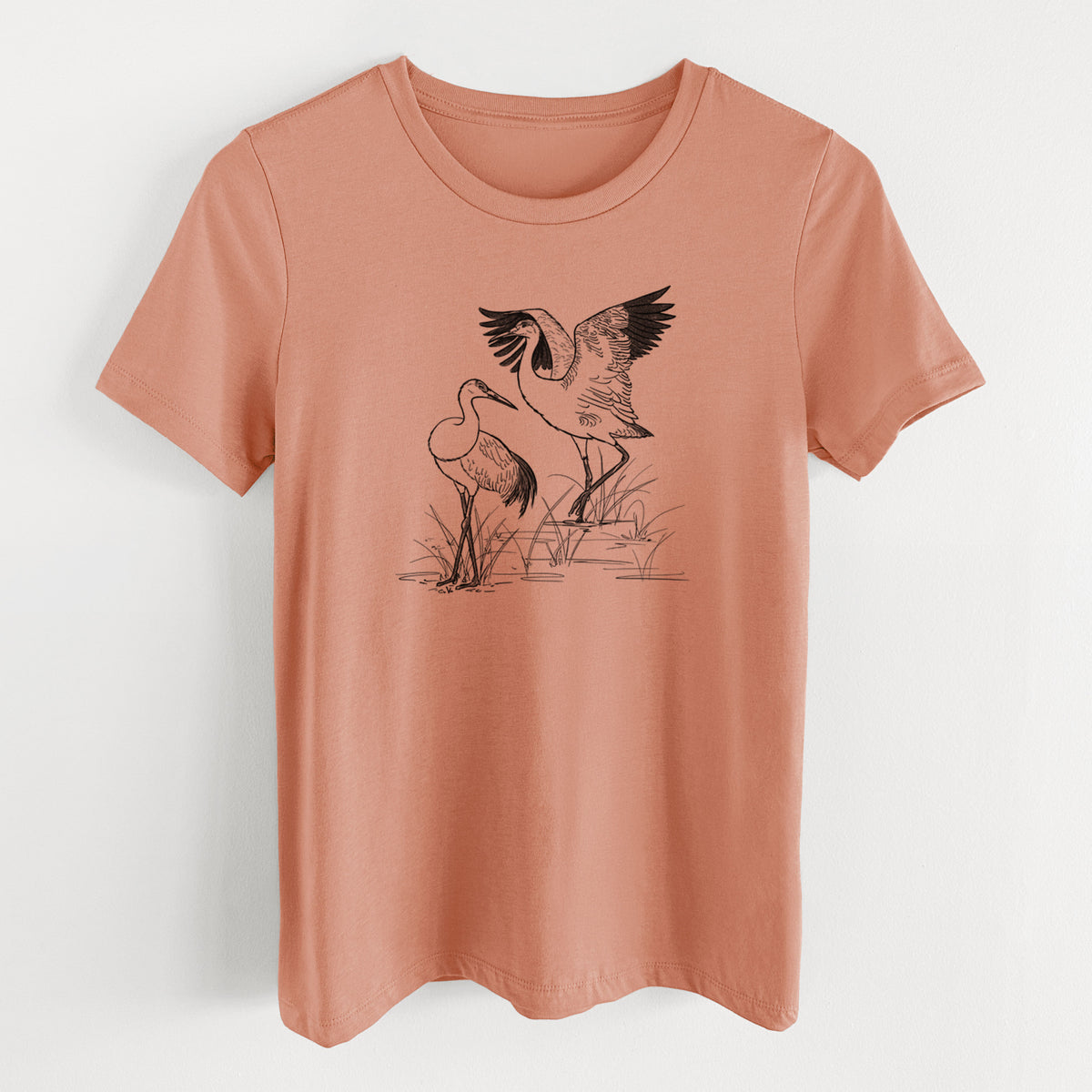 Terracotta orange women's relaxed fit cotton t-shirt laid flat, printed with a black ink illustration of two sandhill cranes in marsh grass, one with its wings raised.