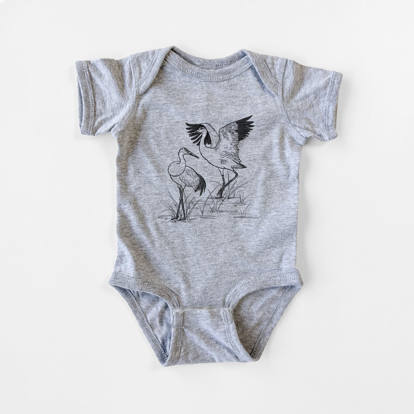 Grey baby bodysuit laid flat, printed with a black ink illustration of two sandhill cranes in marsh grass, one with its wings raised.