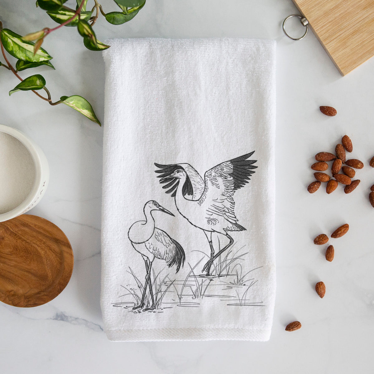 White hand towel printed with a black ink illustration of two sandhill cranes in marsh grass, one with its wings raised.