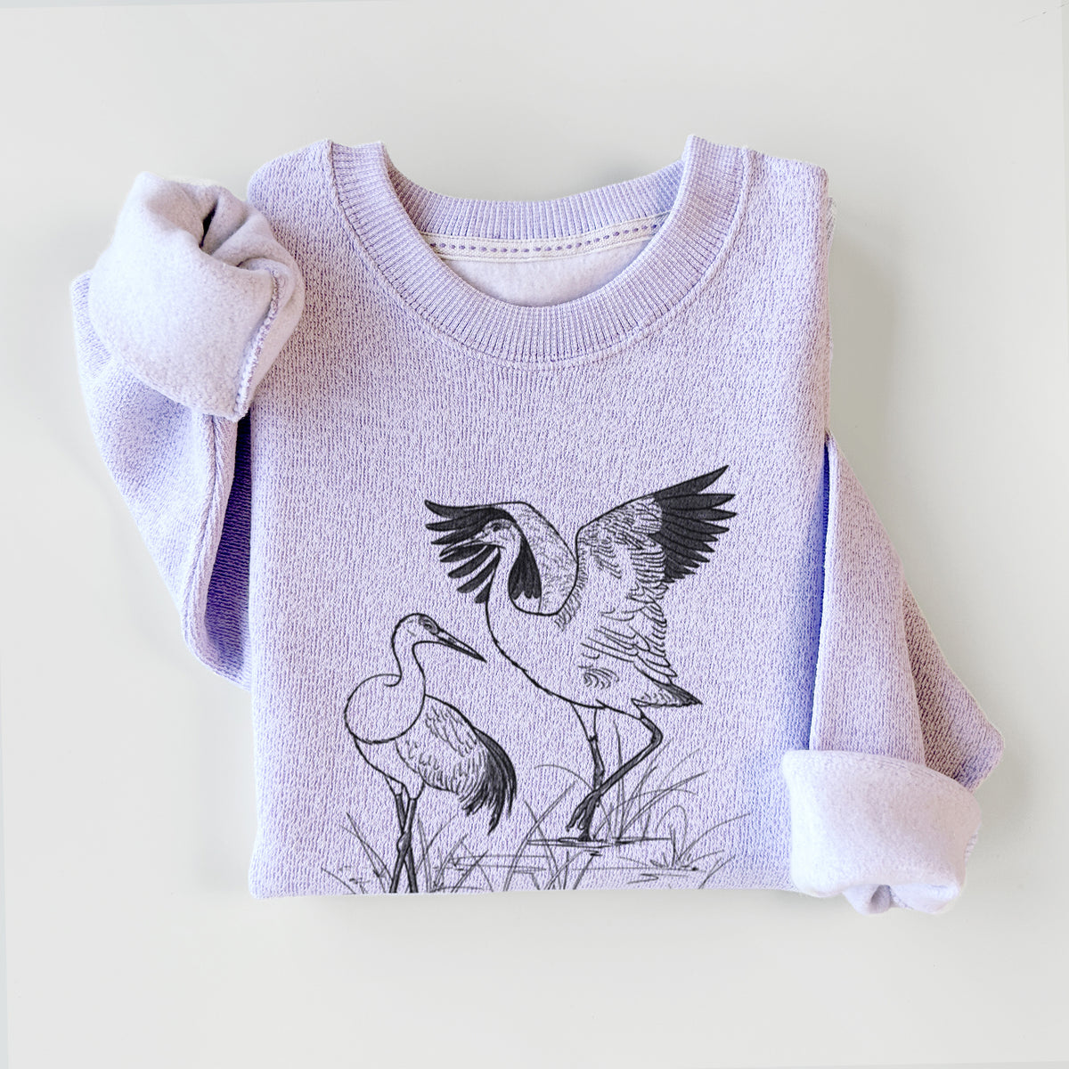 Ice purple knit sweatshirt printed with a black ink illustration of two sandhill cranes in marsh grass, one with its wings raised, styled flat.