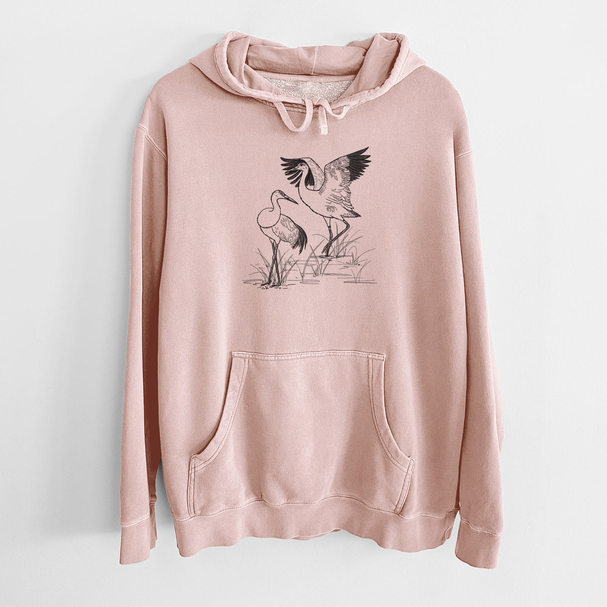 Dusty pink pigment dyed hoodie laid flat, printed with a black ink illustration of two sandhill cranes in marsh grass, one with its wings raised.