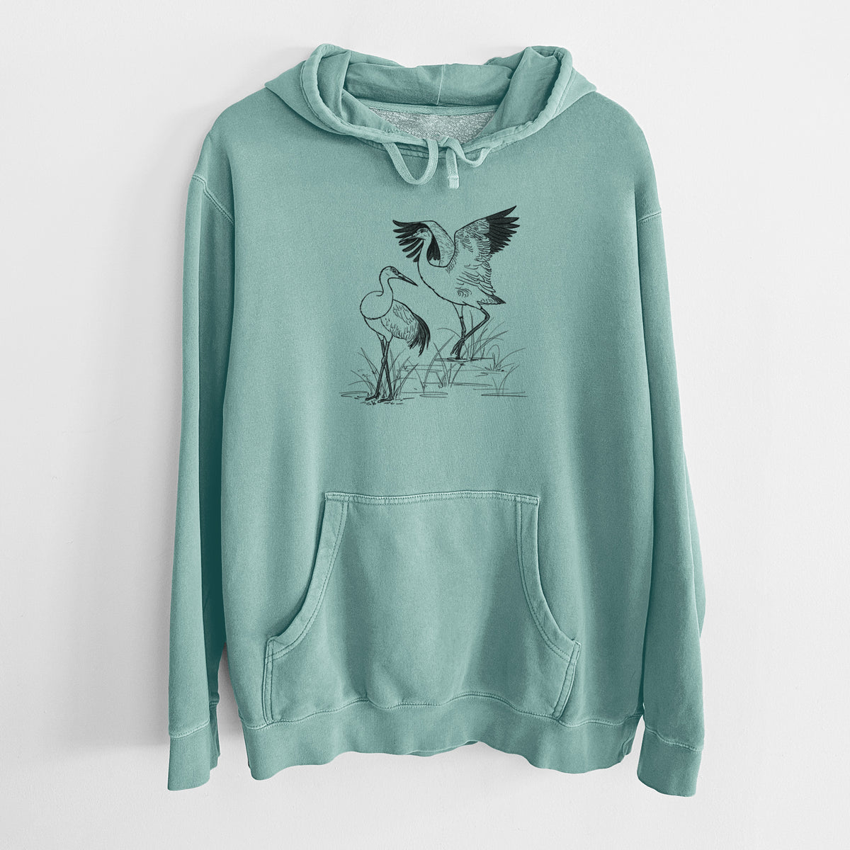 Mint green pigment dyed hoodie laid flat, printed with a black ink illustration of two sandhill cranes in marsh grass, one with its wings raised.