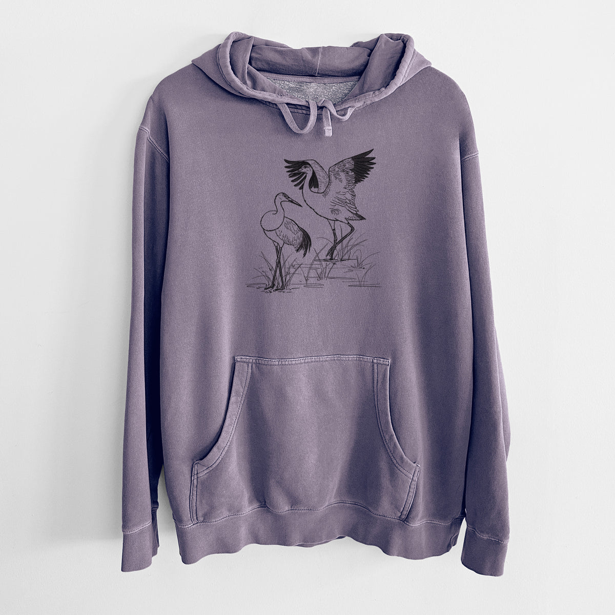Plum purple pigment dyed hoodie laid flat, printed with a black ink illustration of two sandhill cranes in marsh grass, one with its wings raised.