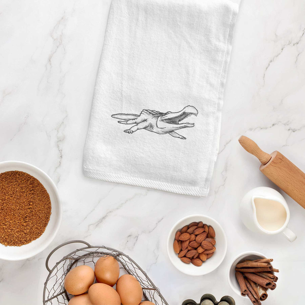 White hand towel printed with a black ink illustration of a Sarcosuchus, a giant prehistoric crocodile, hanging on a cabinet door.