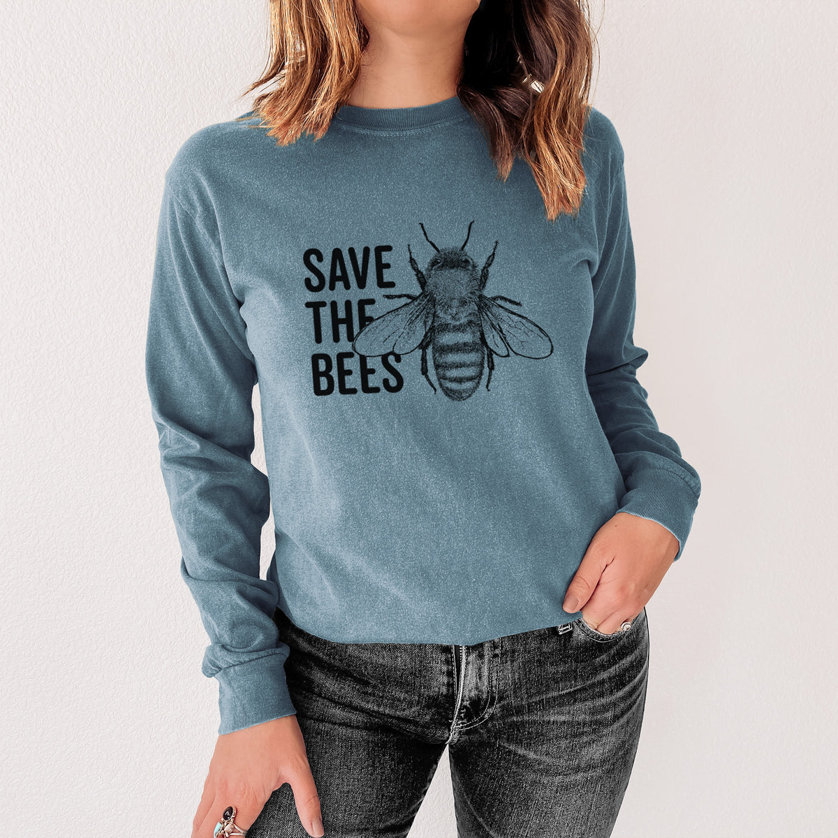 Steel blue Comfort Colors long sleeve shirt printed with bold black words reading Save the Bees beside a detailed honey bee illustration, shown in a lifestyle photo.
