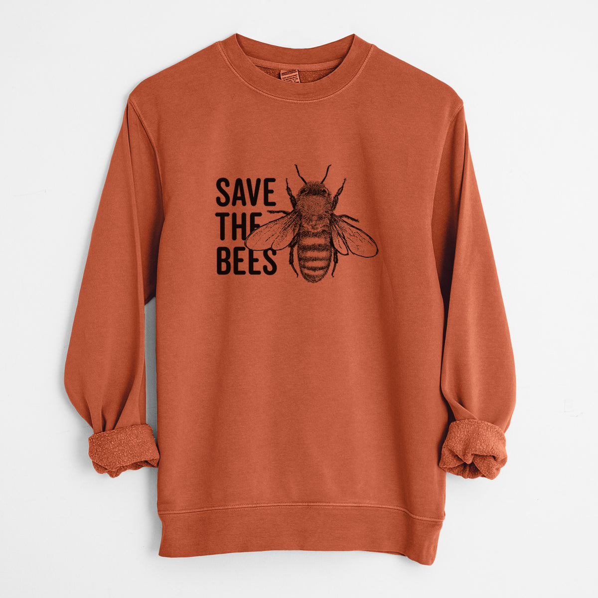 Amber orange pigment dyed crewneck sweatshirt laid flat with the sleeves rolled, printed with bold black words reading Save the Bees beside a detailed honey bee illustration.