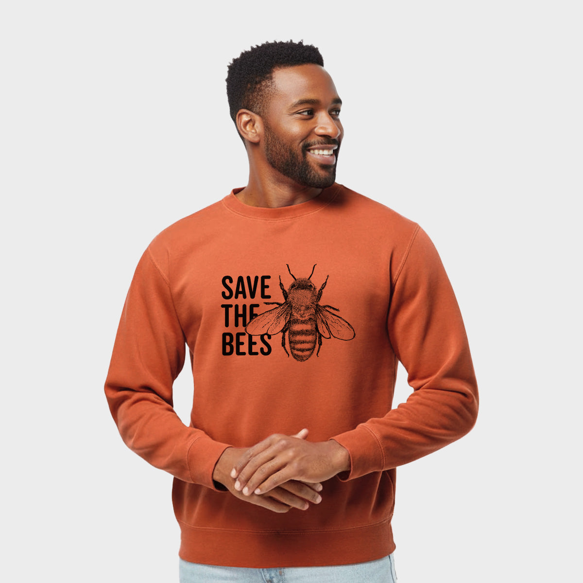 Model wearing an amber orange pigment dyed crewneck sweatshirt printed with bold black words reading Save the Bees beside a detailed honey bee illustration.