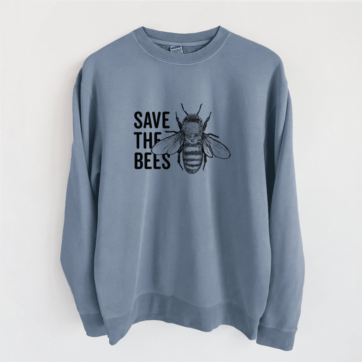 Slate blue pigment dyed crewneck sweatshirt laid flat, printed with bold black words reading Save the Bees beside a detailed honey bee illustration.