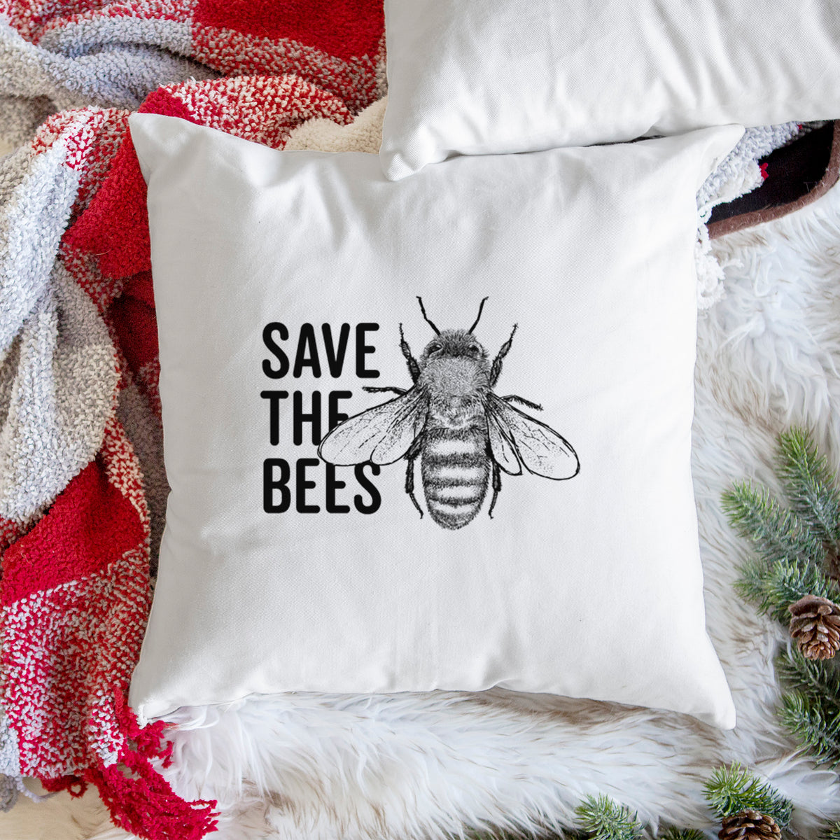 White pillow cover printed with bold black words reading Save the Bees beside a detailed honey bee illustration, on a woven chair.