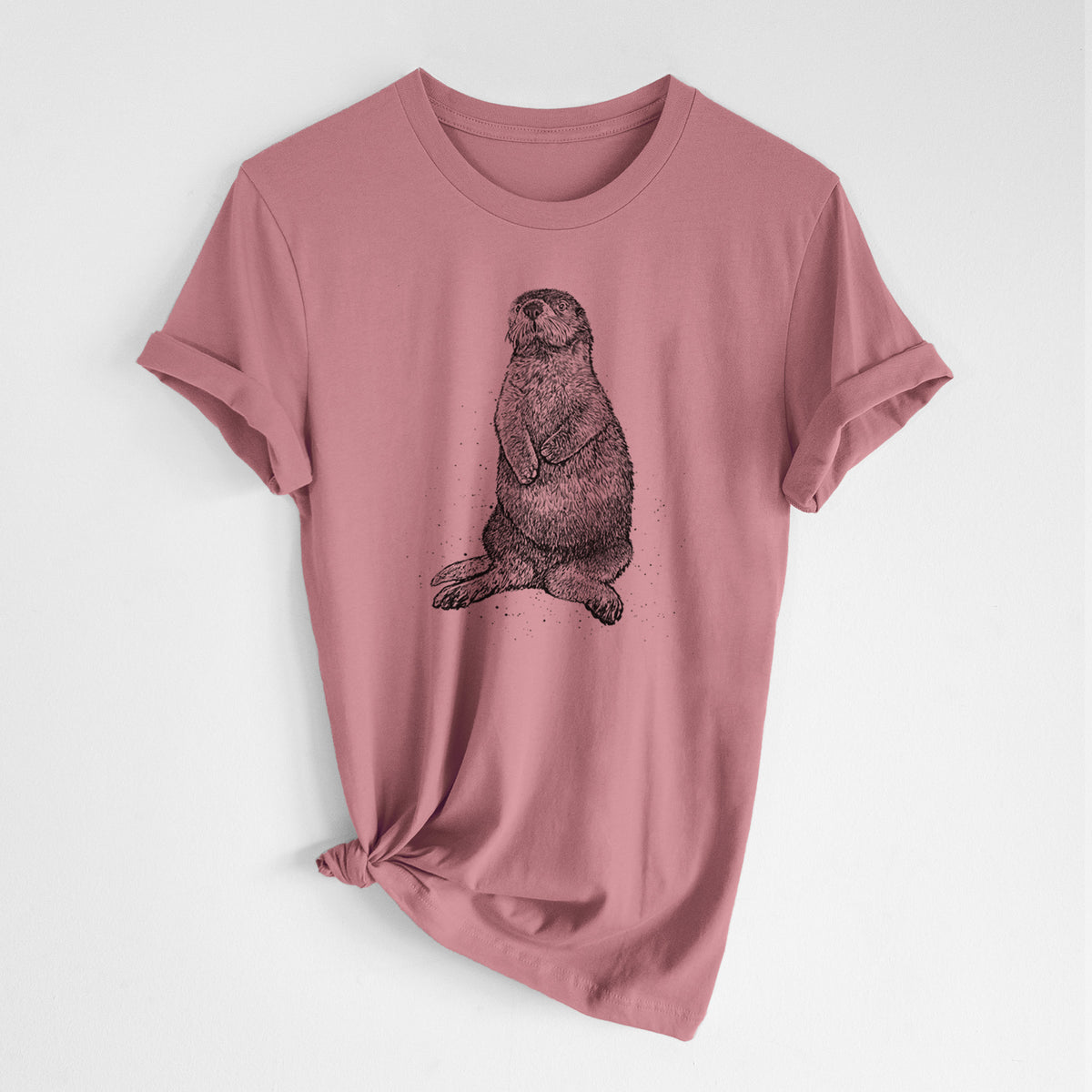 Mauve pink lightweight cotton t-shirt laid flat with the sleeves rolled, printed with a detailed black ink illustration of a sea otter sitting upright.