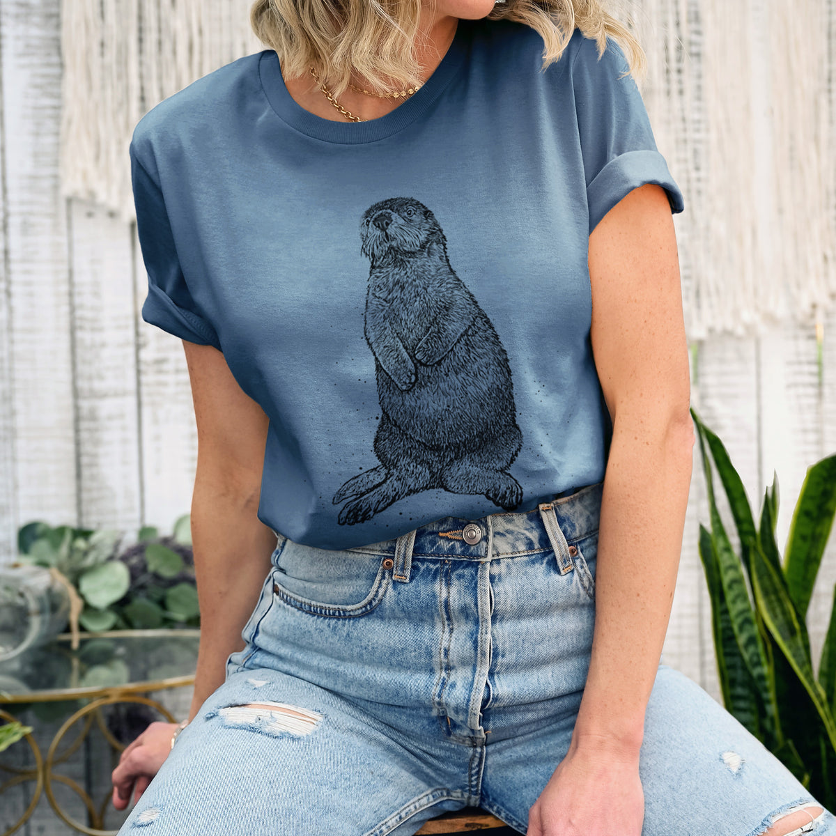 Woman wearing a steel blue lightweight cotton t-shirt printed with a detailed black ink illustration of a sea otter sitting upright.