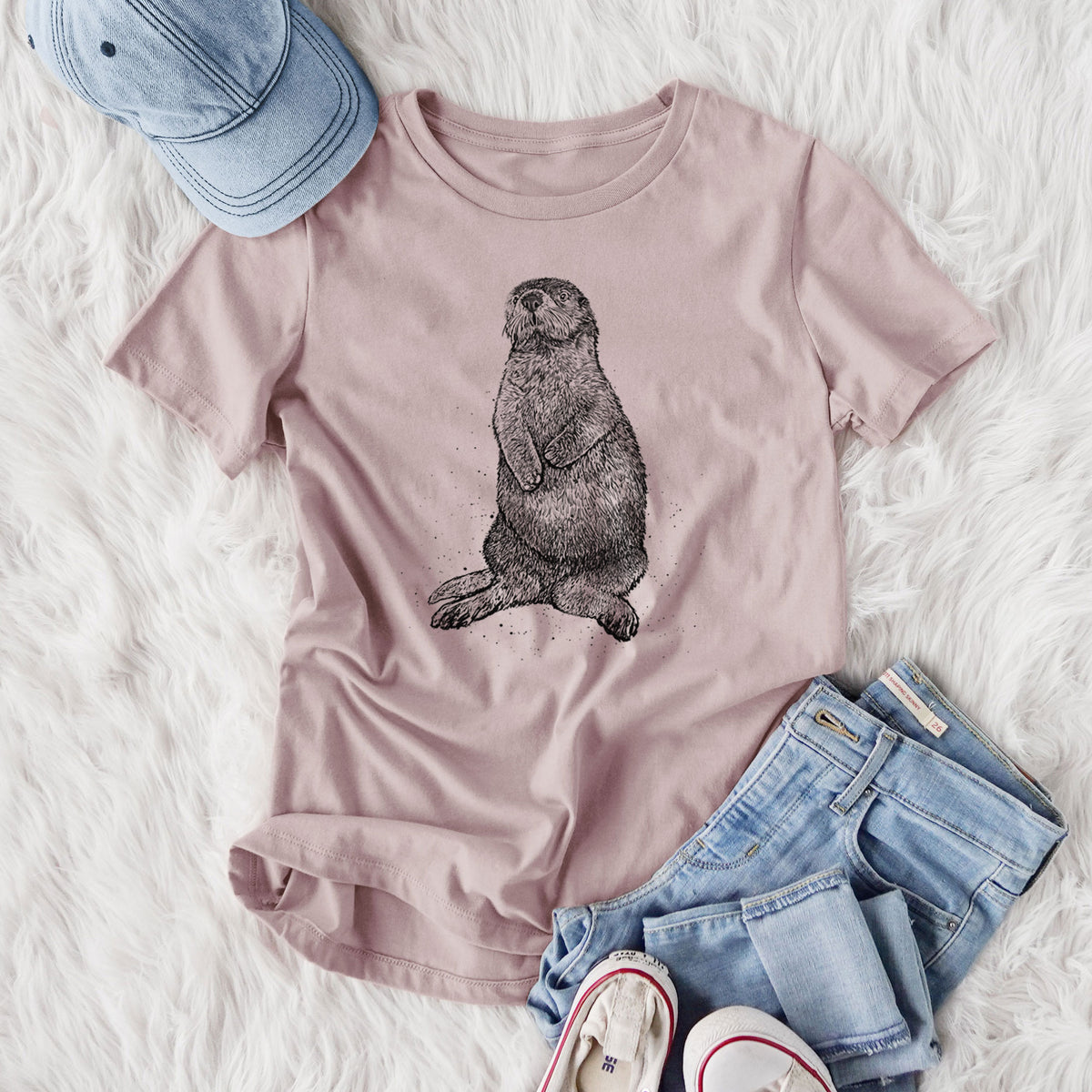 Women's relaxed fit cotton t-shirt printed with a detailed black ink illustration of a sea otter sitting upright, styled flat on a white faux fur rug with jeans.