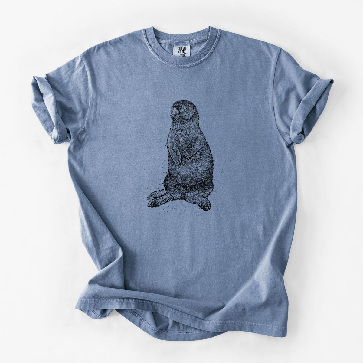 Blue jean Comfort Colors t-shirt laid flat, printed with a detailed black ink illustration of a sea otter sitting upright.