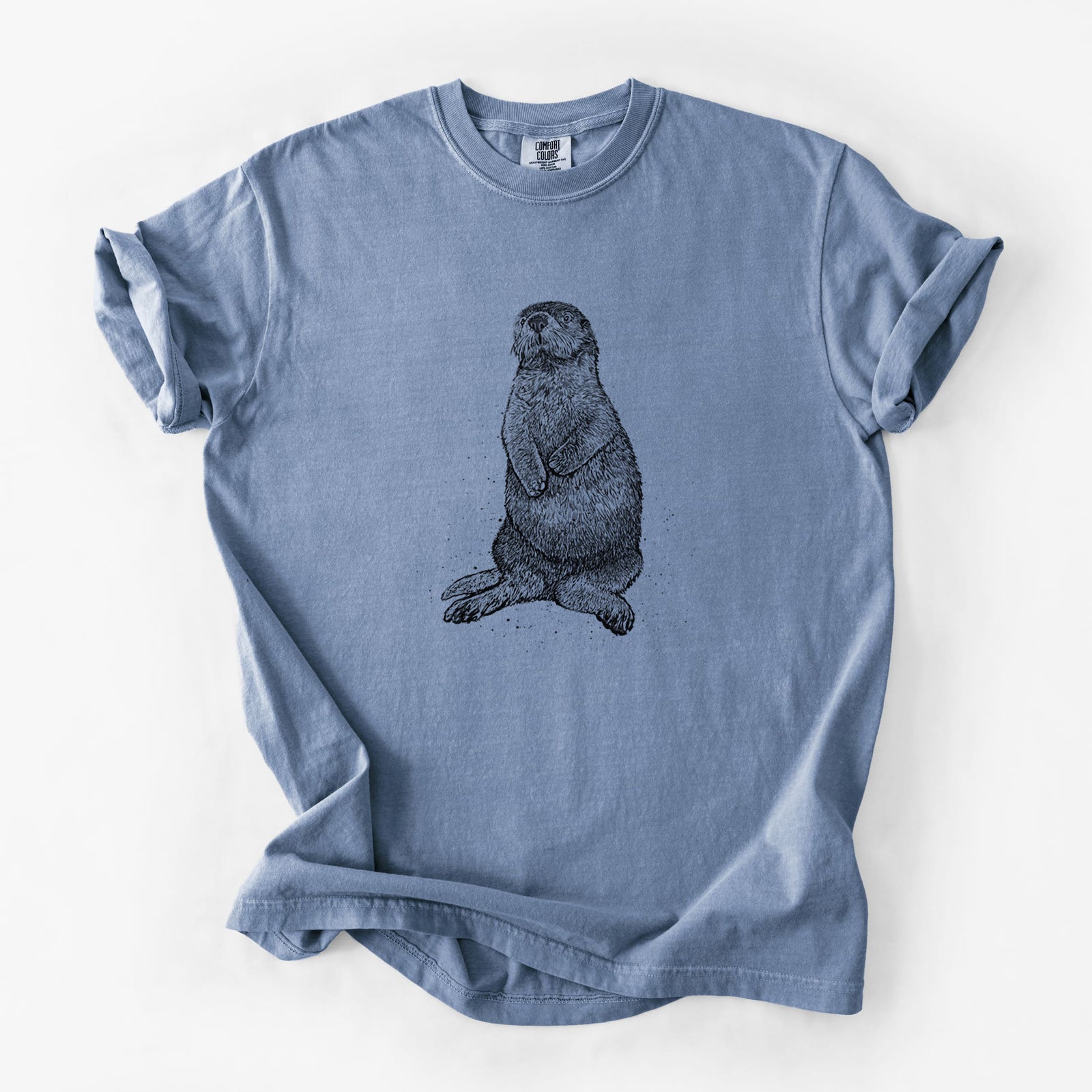 Blue jean Comfort Colors t-shirt laid flat, printed with a detailed black ink illustration of a sea otter sitting upright.