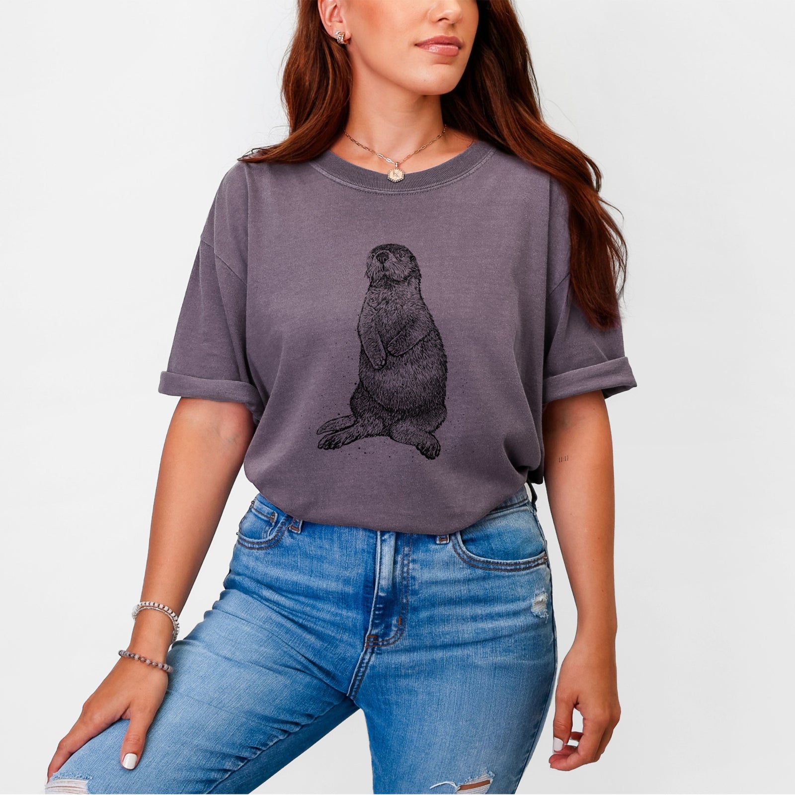 Blue jean Comfort Colors t-shirt laid flat, printed with a detailed black ink illustration of a sea otter sitting upright.