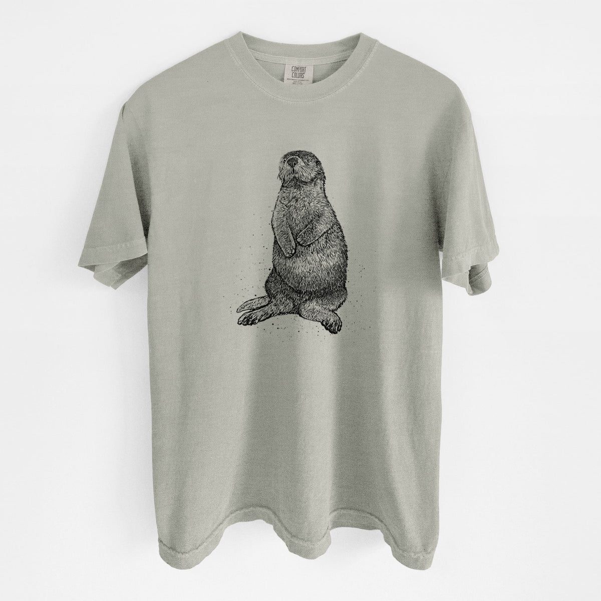 Sandstone beige Comfort Colors t-shirt laid flat, printed with a detailed black ink illustration of a sea otter sitting upright.