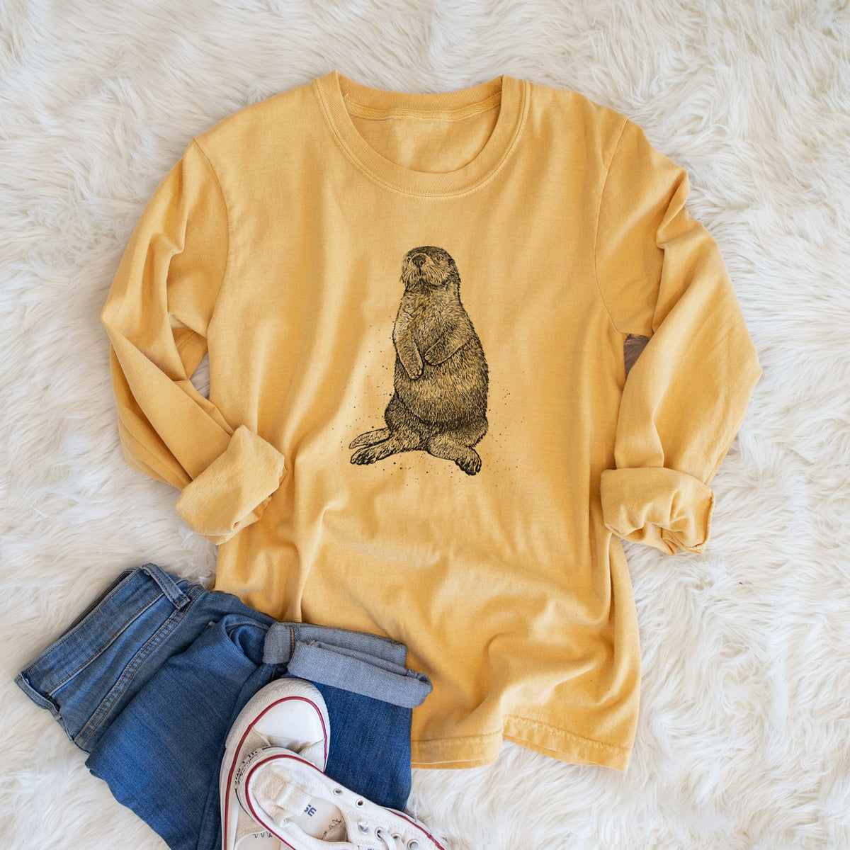 Golden wheat yellow Comfort Colors long sleeve shirt printed with a detailed black ink illustration of a sea otter sitting upright, shown in a lifestyle photo.