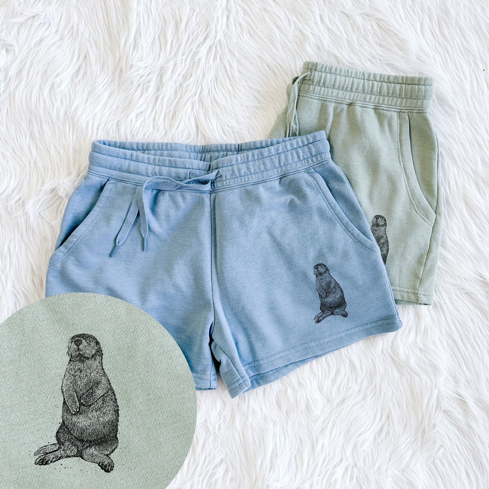Two pairs of Cali Wave shorts in different colors printed with a detailed black ink illustration of a sea otter sitting upright, with a close-up of the print.