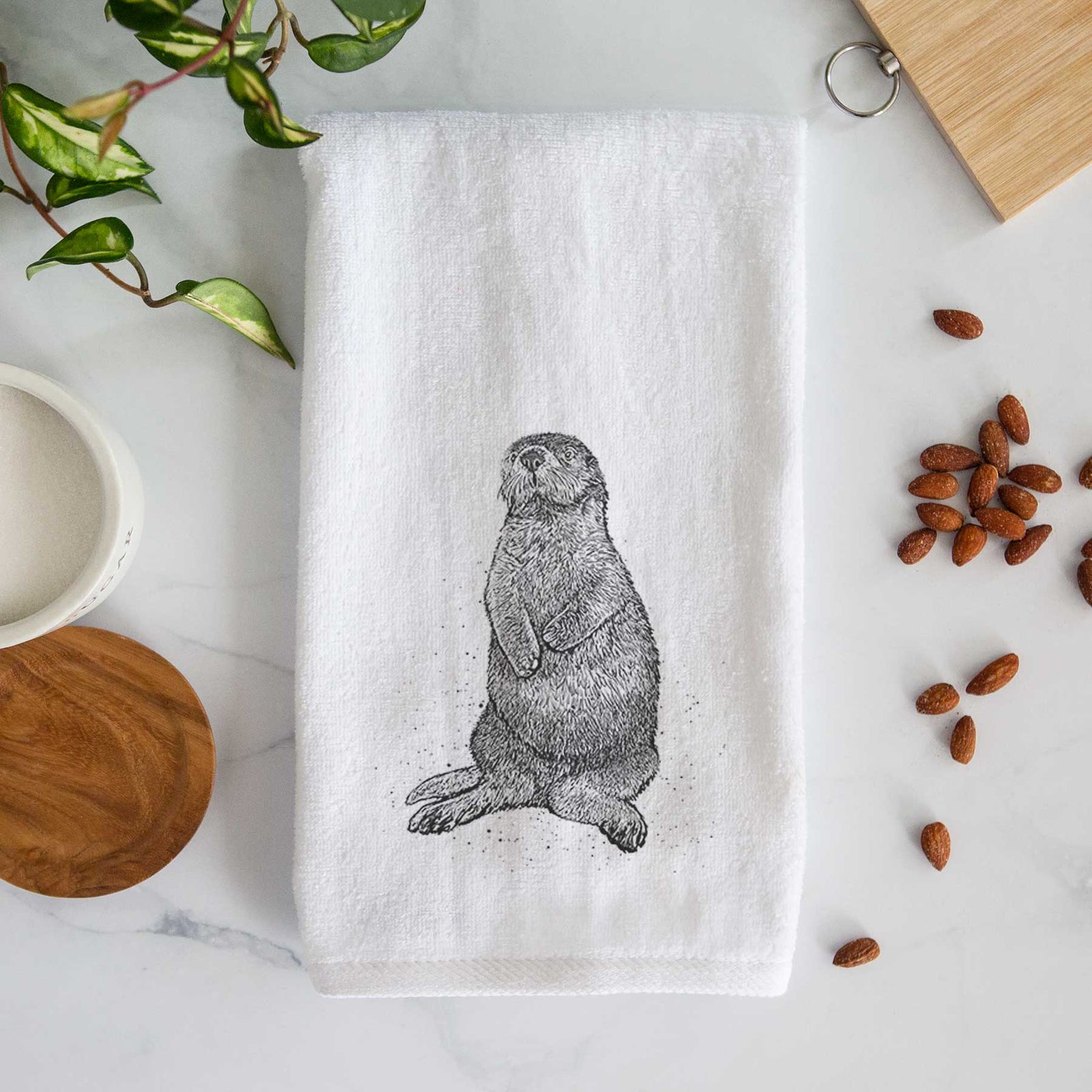 White hand towel printed with a detailed black ink illustration of a sea otter sitting upright.