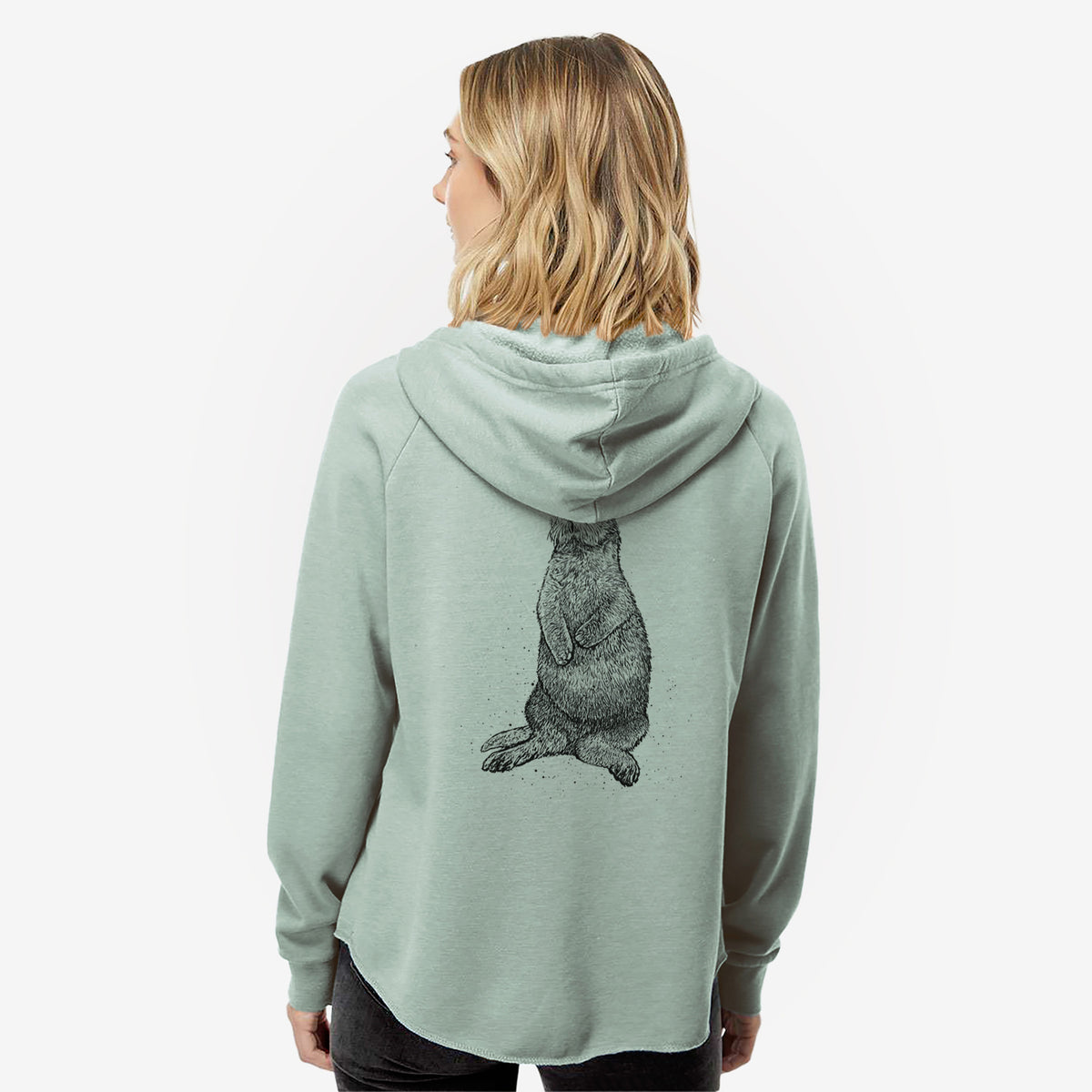 Woman wearing a sage green women's Cali Wave zip-up sweatshirt printed with a detailed black ink illustration of a sea otter sitting upright, seen from behind.