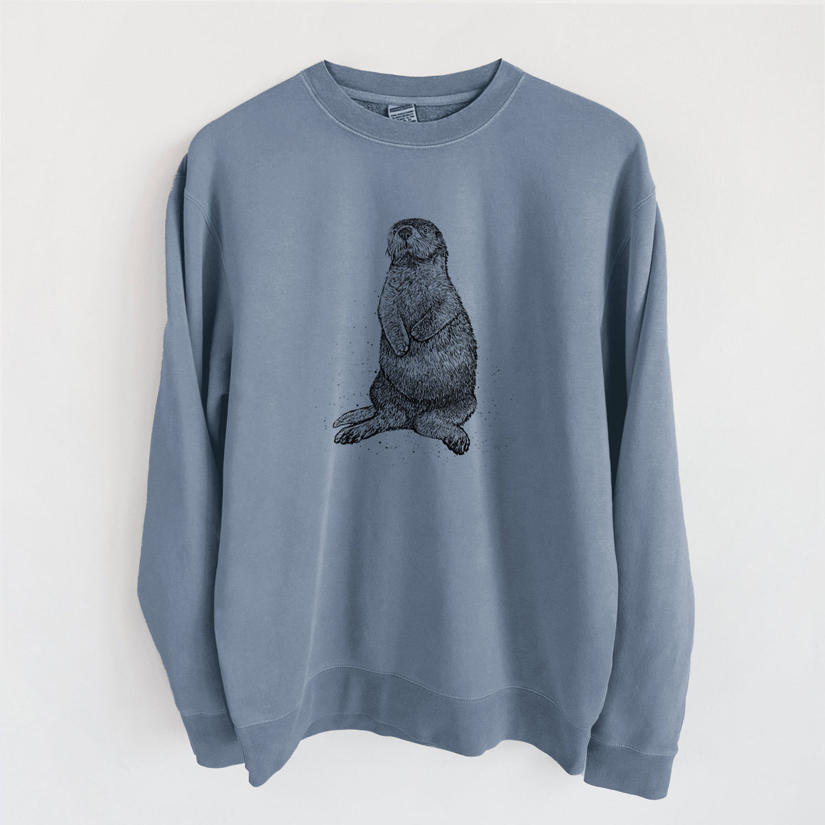 Slate blue pigment dyed crewneck sweatshirt laid flat, printed with a detailed black ink illustration of a sea otter sitting upright.